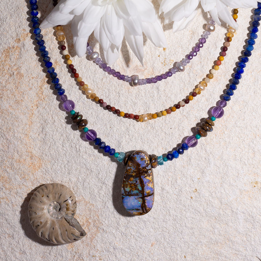 This Australian opal pendant has incredible colours, pale icy blue and some bright green sprinkle across an ancient landscape crisscrossed with deep gullies . A solid opal with the intensity of bright colour that is absolutely unique, on a deep blue Lapis Lazuli faceted bead necklace.