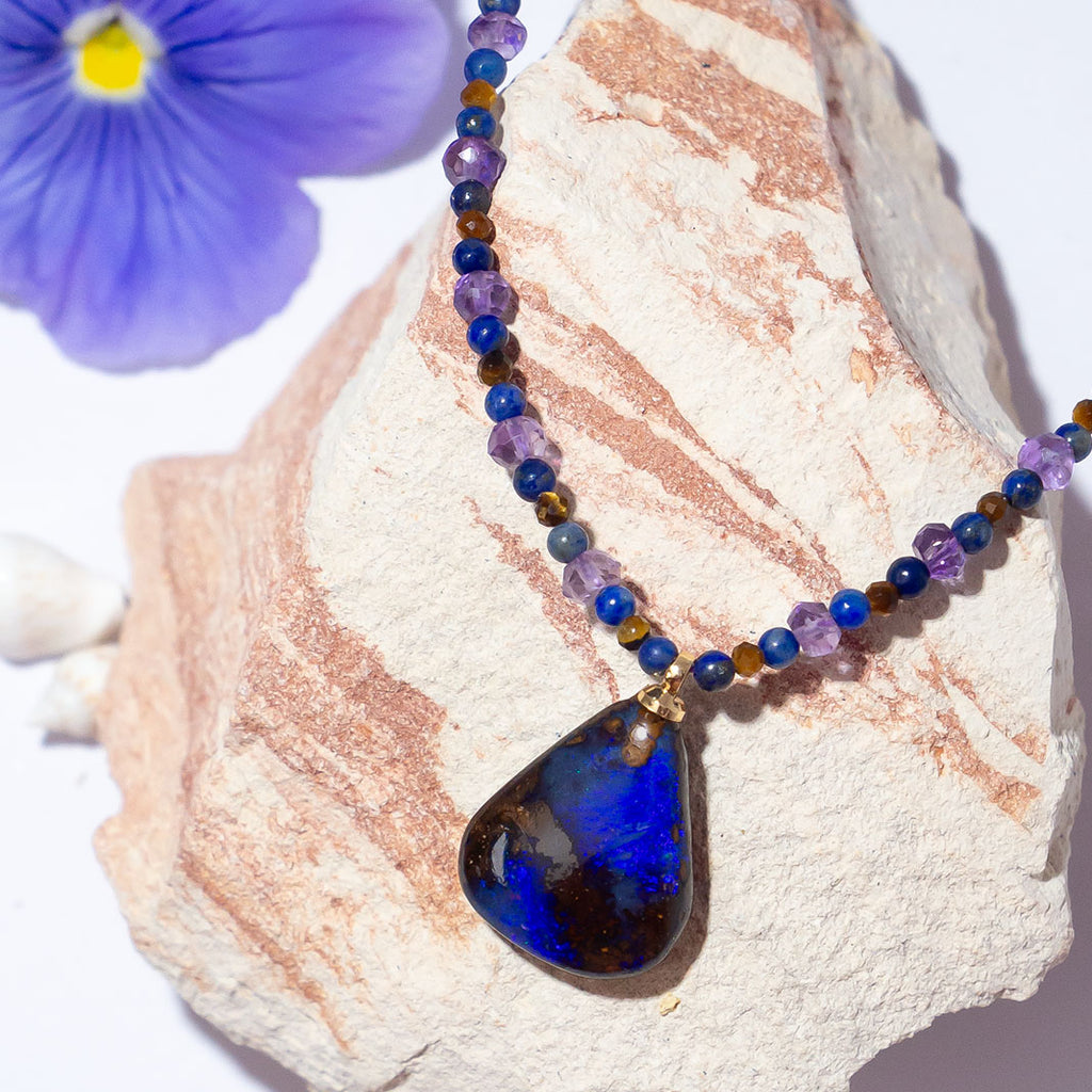 With beautiful pools of dark blue colour play found within the deep brown boulder stone this enthralling opal is complimented by the jewel tones of amethyst, lapis lazuli & shimmering tigers eye.